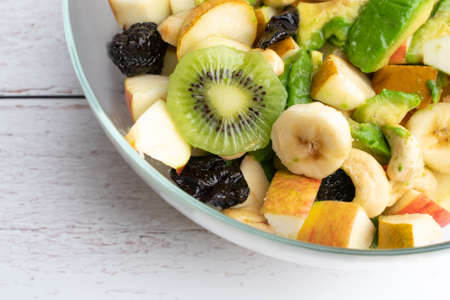 Studio shot of glass bowl with freshly made fruit salad in it on a white wooden table. Healthy eating concept. Vegetarian food. Vegan raw diet. Assorted fruits mixed in a bowl.の写真素材