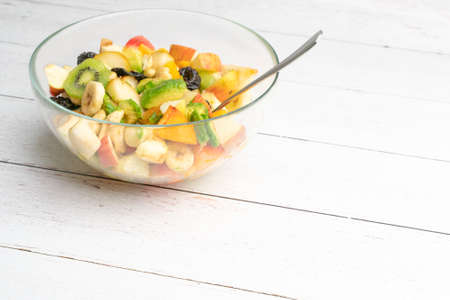 Studio shot of glass bowl with freshly made fruit salad in it on a white wooden table. Healthy eating concept. Vegetarian food. Vegan raw diet. Assorted fruits mixed in a bowl.の写真素材