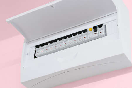 Detail of opened home white fuse box with set of black electric fuses. Pink wall in the back. Electricity and safety.の写真素材