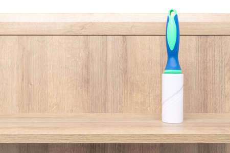 Adhesive pet hair remover roller standing vertical on a wooden board. Green and blue color of the...