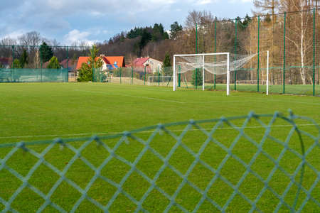 Village soccer field of a minor league on a nice sunny day of spring. Fence in front. Amateur sport arena. Soccer goal with white posts.の写真素材