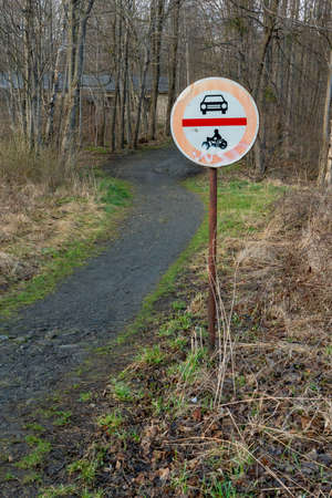 No cars and no motorcycles sign next to a trail leading to a forest on a cloudy day of spring. Traffic sign in remote rural area.の写真素材