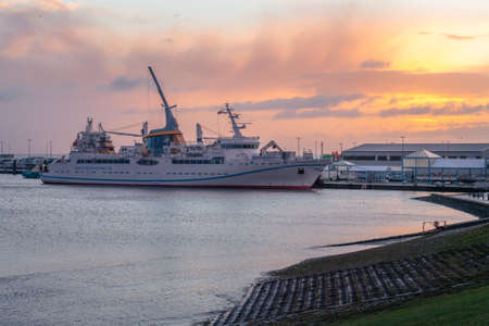 Cuxhaven, Germany - 02.25.2022: Sunrise by the sea with Helgoland ferry docked in the port of Cuxhaven. Sky glowing in orange and yellow. Golden hour in the north.のeditorial素材