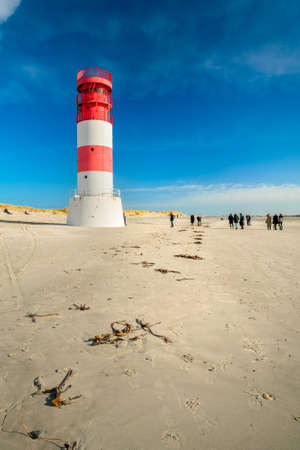 Dune and Heligoland, Germany - 02.27.2022: Vertical shot of people walking around lighthouse on the beach of Dune island, Heligoland, on a beautiful sunny winter day with blue sky.のeditorial素材