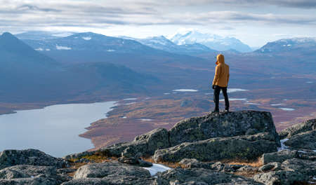 Male hiker overlooking epic view of vast arctic landscape of Stora Sjofallet National Park, Sweden, on autumn day. Mountains and valleys of Lapland. Ahkka massif. View from the top of Lulep Gierkav.の写真素材