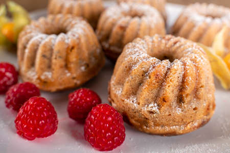 Lovely sweet cakes on white plate with sugar on top, raspberries and golden berries below. Homemade baked sweets for snack or breakfast.の写真素材