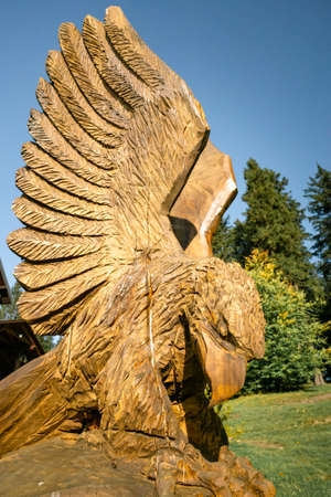 Detail shot of wooden sculpture of bird of prey with trees and blue sky in the background.の写真素材