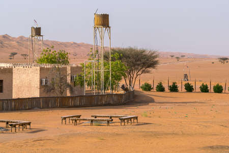 Wahiba Sands, Oman - 04.03.2018: Clay buildings in Arabian desert. Small trees and water towers. Adventure in Wahiba Sands desert. Travel Arabia.のeditorial素材