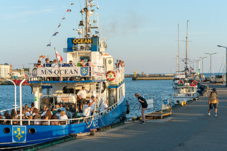 Hel, Poland - 08.04.2022: Shot of blue and white MS Ocean tourist boat leaving the pier on a beautiful sunny summer day with Baltic sea and blue sky in the background. Lot of people aboard.のeditorial素材