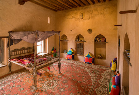 Nakhal, Oman - 04.03.2018: Room of a medieval arabian castle. Carpets and pillow on the floor, holy books on the shelf. Fancy bed. Fort of Nakhal, Oman.のeditorial素材