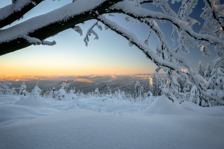 Yellow glow on a distant horizon above Little Fatra mountains on a cold day of winter with lots of snow. Vast forests covered in frost and snow. Beautiful winter day in the mountains.の写真素材