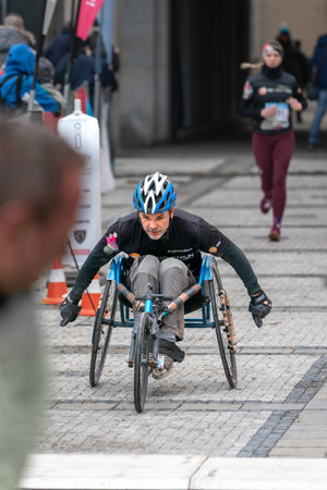 Ostrava, Czechia - 02.04.2023: Vertical shot of middle aged disabled man wearing helmet in a sports wheelchair competing during a winter run race in a city. Innogy winter run.のeditorial素材