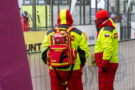 Ostrava, Czechia - 02.04.2023: Two male security medics in bright green reflective vests overlooking run race competition in the city. Innogy winter run race.のeditorial素材