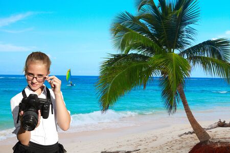 Young girl, reflex camera and tropical palm on blue sky background. Exotic vacationの写真素材