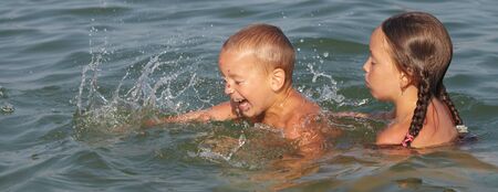 Little boy and girl playing in the water in the seaの写真素材