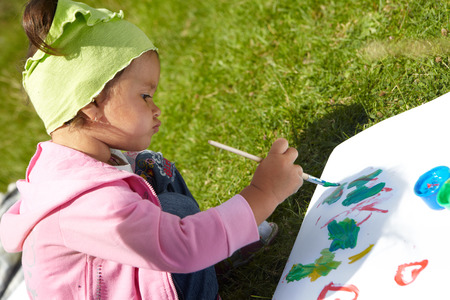 Little girl draws paints on a green lawnの写真素材