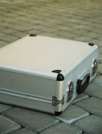 Locked metal suitcase is lying on the pavement