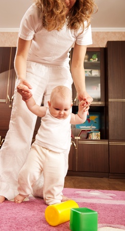 Young mother is helping her daughter to make first stepsの写真素材