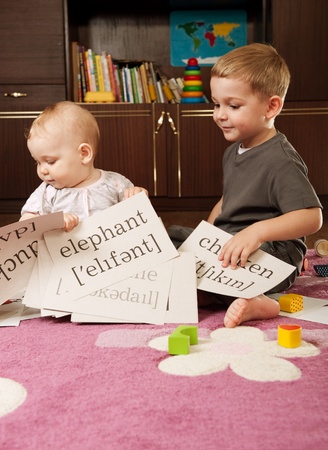 A boy aged three and a girl aged one are playing with blocks and cards with wordsの写真素材