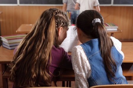 Two schoolgirls chating in classromm during lessonの写真素材