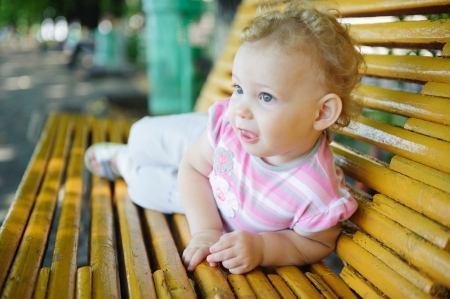 Cute curly haired baby girl on bench at parkの写真素材