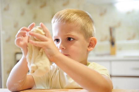 Concentrated little boy kneading dough in the kitchenの写真素材