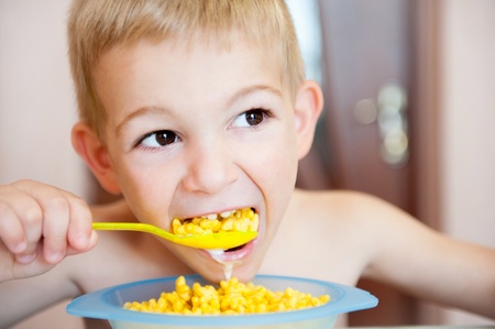 Little blond boy eating corn flakes with milk