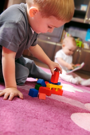 Cute kid playing with colorful cubes on the floor. His sister on background.の写真素材