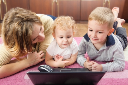 Young mother with her son and daughter lying on floor with laptop. Front view.の写真素材