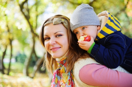 Young mother with her little son eating apple in autumn parkの写真素材