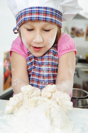 Little girl in hat and apron cooking in kitchenの写真素材