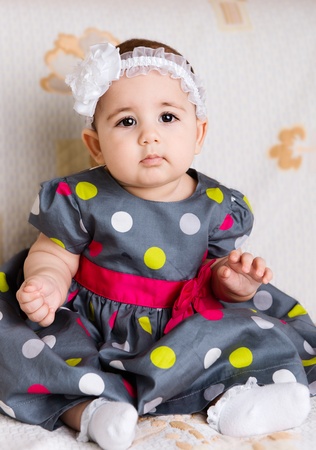 Cute baby girl in dotted dress sitting on sofaの写真素材