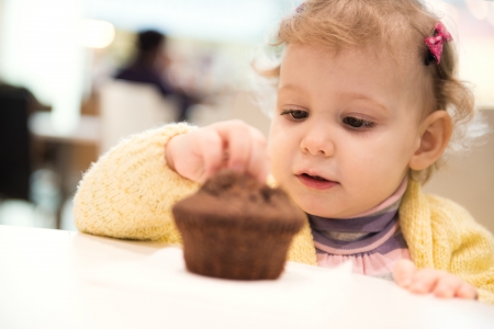 Cute little girl eating muffins in cafeの写真素材
