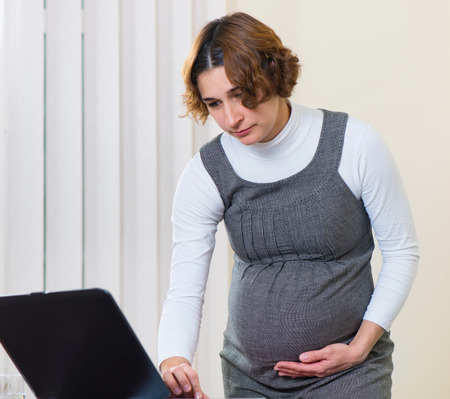 Young pregnant woman in dress working at officeの写真素材