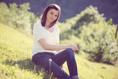 Pretty young woman posing on green sunny lawn in mountainsの写真素材