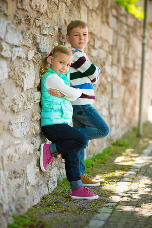 Two cute children standing near the stone wallの写真素材