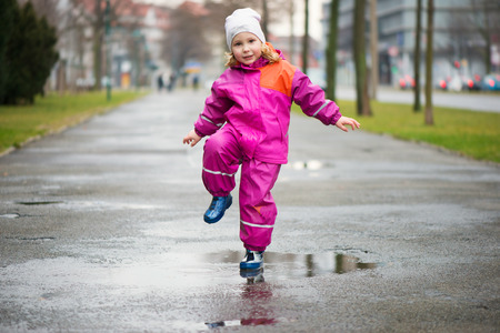 Little happy girl jumping and having fun in puddleの写真素材