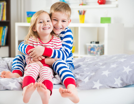 Two happy siblings in striped sleepwears in bedの写真素材