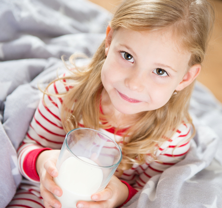 Cute little girl with glass of milk in bedrromの写真素材