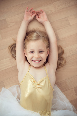 Pretty smiling ballet chilg girl in white tutu lying on floorの写真素材