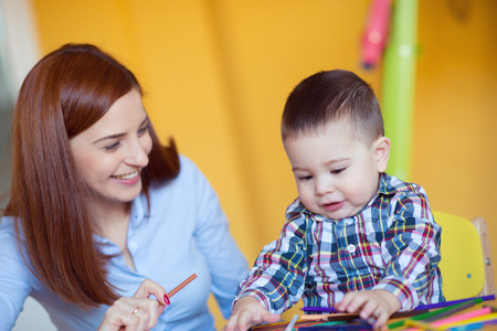 Portrait of happy pretty mother with her toddler son drawing with pencils