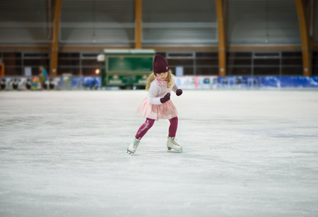 Pretty little girl skates in a red cap, warm gloves and sweaterの写真素材