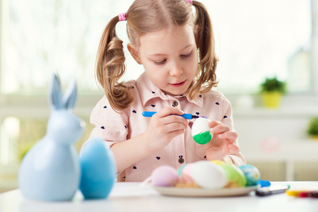 Happy pretty child girl having fun during painting eggs for easter in spring at homeの写真素材