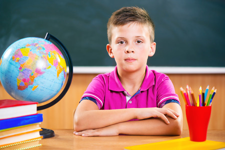 Cute diligent boy sitting in classroom in front of blackboardの写真素材