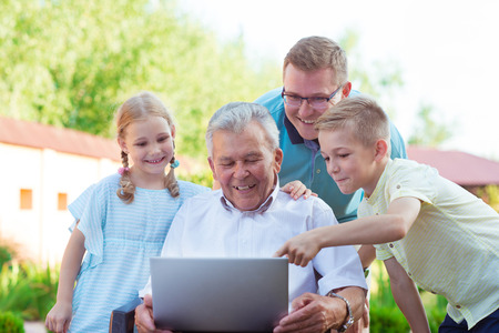 Happy family with grandfather having fun during internet talking on laptopの写真素材