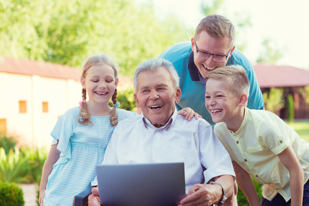 Happy family with grandfather having fun during internet talking on laptop