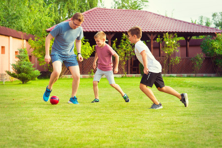 Two happy sons playing football with their father in garden near modern House