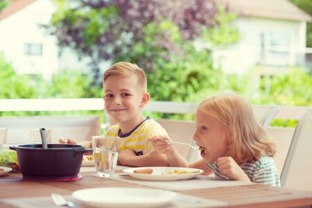 Two happy little children eating healthy breakfast on terrace at homeの写真素材