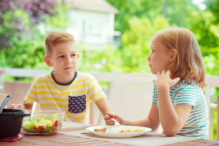 Two happy little children eating healthy breakfast on terrace at homeの写真素材