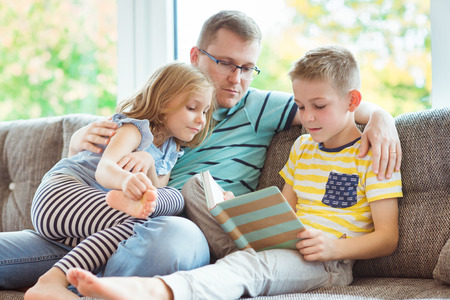 Young happy father reading book with two cute children at homeの写真素材